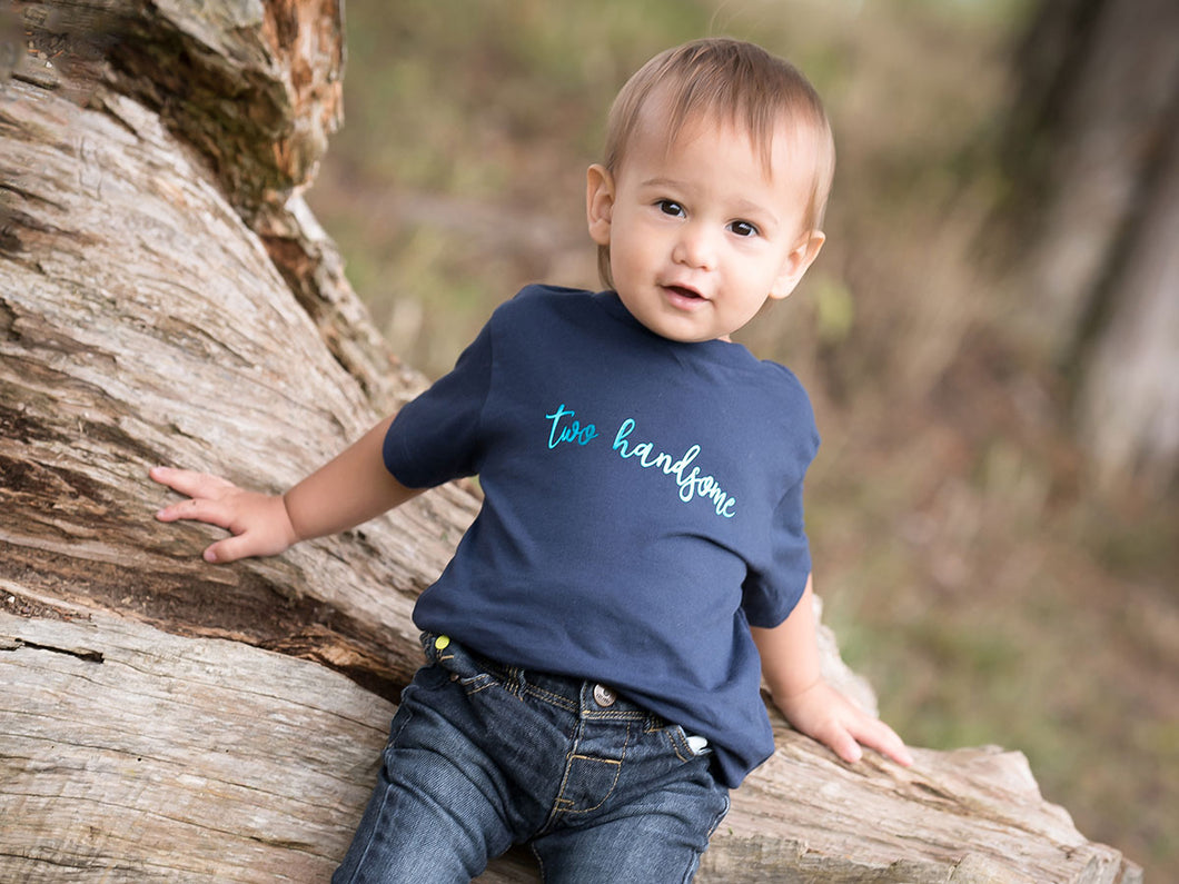 Two Handsome navy t-shirt by Little Foxglove modelled on a toddler, sat outside on a tree